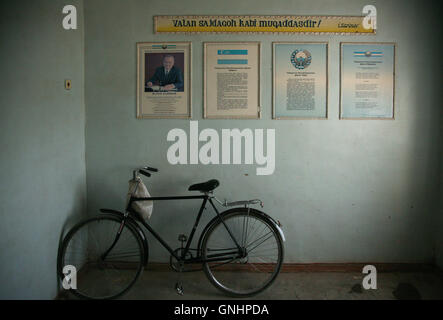 Ein Fahrrad geparkt neben dem Porträt des usbekischen Präsidenten Islom Karimov in der Zahnklinik in Khorezm Region, Chiwa, Usbekistan. Die Nationalflagge der Republik Usbekistan, das Wappen der Republik Usbekistan und die Nationalhymne der Republik Usbekistan sind abgebildet und beschrieben in den Frames neben dem Porträt. Stockfoto