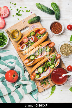 Homemade Hot Dogs auf hölzernen servieren mit frischem Gemüse, Gewürze, Ketchup und Senf über weißen gemalten Hintergrund, top Stockfoto