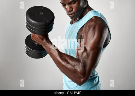 Schuss von Fit junge Mann tut Bizeps curl mit Hantel vor grauem Hintergrund. Training mit schweren Dumbb afrikanische Fitness-Modell Stockfoto