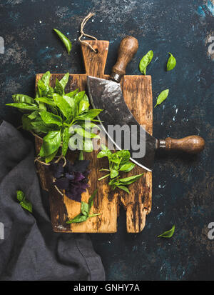 Frische Basilikumblätter grüne und violette mit Kraut Chopper Messer auf rustikale Schneidbrett über Grunge dunkel blau Sperrholz Textur. Top v Stockfoto