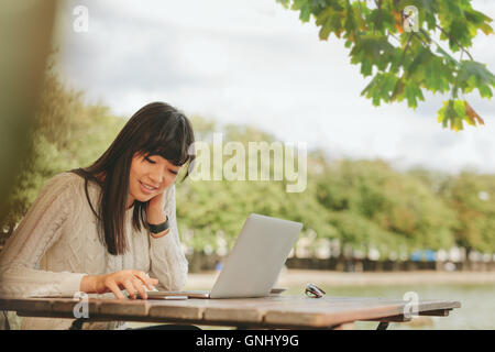 Schuss von glücklich Asiatin mit Smartphone auf Outdoor-Coffee-Shop. Frau mit Laptop im Freien mit Mobil am Café-Tisch sitzen Stockfoto