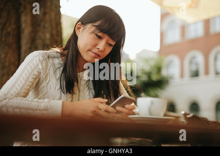 Chinesische Frau Textmitteilung auf smart Phone in einem Café zu schreiben. Bild junge Frau sitzt an einem Tisch mit einem Kaffee mit mobilen p Stockfoto