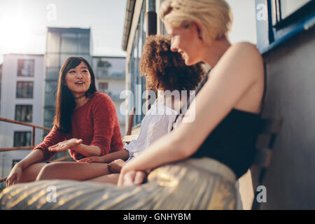 Schuss von jungen weiblichen Freunden beisammen sitzen auf der Terrasse. Gemischtrassig Frauen entspannen im Freien in einen Balkon. Stockfoto