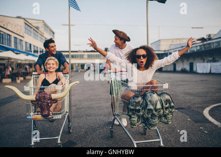 Junge Freunde, die Spaß auf einen Einkaufswagen. Multiethnische Jugendlichen racing auf Warenkorb. Stockfoto