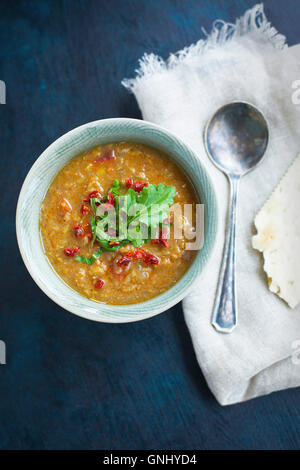 Rote Linsensuppe mit getrockneten Tomaten und Rucola in Keramikschalen gekrönt.   Fotografiert von Draufsicht auf eine dunkle blaue Fläche. Stockfoto