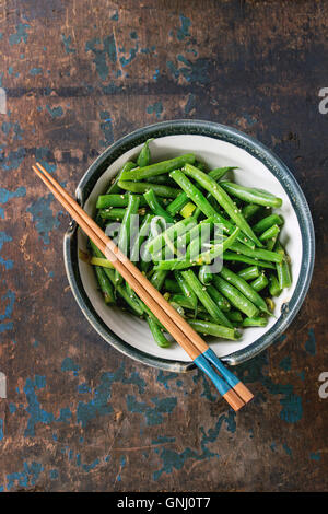 Schüssel mit gebratene grüne Bohnen mit Zwiebeln und Sesam-Samen, serviert mit hölzernen Stäbchen über dunklen hölzernen strukturierten Hintergrund. Asiatische s Stockfoto