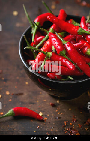 Schwarze Schale mit nasse frische rote scharfe Chilischoten und trockenem Chiliflocken über alte hölzerne strukturierten Hintergrund. Würzige Thema. Nahaufnahme w Stockfoto