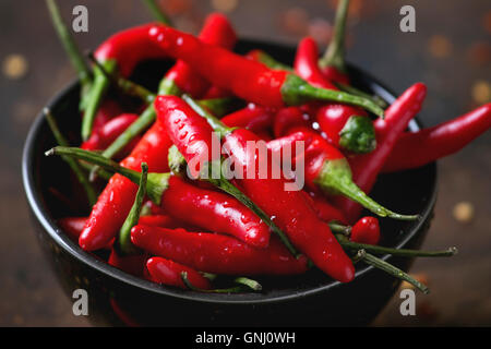 Schwarze Schale mit nasse frische rote scharfe Chilischoten und trockenem Chiliflocken über alte hölzerne strukturierten Hintergrund. Würzige Thema. Nahaufnahme w Stockfoto