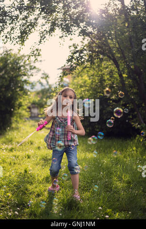 Mädchen bläst Seifenblasen mit Blase Wand im Garten Stockfoto