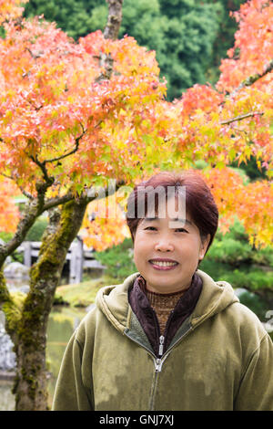 Portrait of Smiling asiatische Frauen mittleren Alters mit Herbstlaub im japanischen Garten im Hintergrund.  Vertical.Copy Raum. Stockfoto