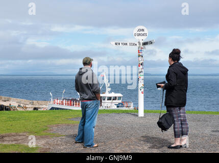 Touristen auf der Suche auf dem berühmten Multi-direktionalen Wegweiser bei John O'Groats, Caithness, Schottland Stockfoto