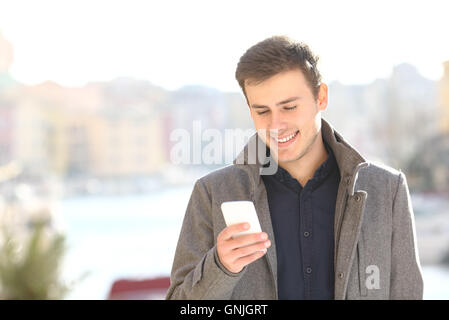 Gut aussehend glücklich lächelnd zu Fuß und mit smart-Phone im winter Stockfoto