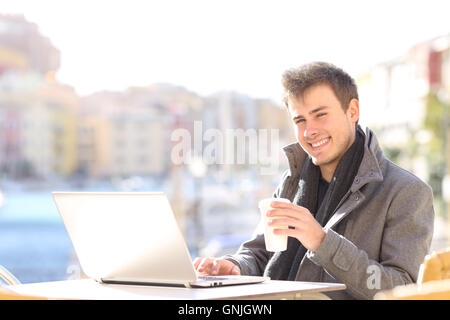 Schöne und elegante Mann mit einem Laptop und Blick in die Kamera in einer Café-Terrasse im Winter in einem Hafen der Urbanisierung Stockfoto