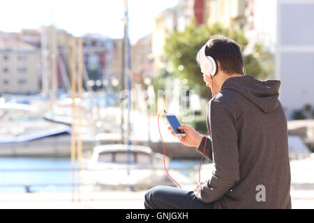 Rückansicht des ein Teenager Musik hören mit Kopfhörern über ein Smartphone auf eine Ferien-destination Stockfoto