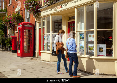 Zwei Frauen auf der Suche in Immobilienmakler Fenster in Ashbourne Derbyshire mit roten Telefon Box und Red Telephone box im Hintergrund Stockfoto