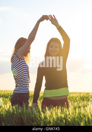 zwei junge Mädchen, die Spaß im Weizenfeld im Sonnenuntergang Stockfoto