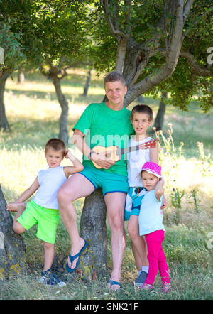 junger Vater spielt Gitarre für seine Kinder auf die Natur. Stockfoto