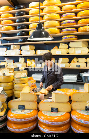 Regalen der Käselaibe und Frau schneiden Käse Keil am Käseladen ' t Kaaswinkeltje in Gouda, Holland, Niederlande Stockfoto