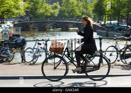Junge Frau trägt high Heels Schuhe tragen iPhone Radfahren heraus für den Abend über Brücke in Amsterdam, Holland Stockfoto