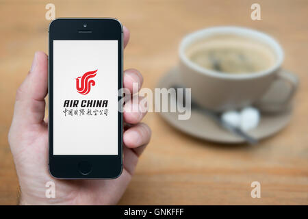 Ein Mann schaut auf seinem iPhone die Air China-Logo anzeigt, während bei einer Tasse Kaffee (nur zur redaktionellen Verwendung) saß. Stockfoto