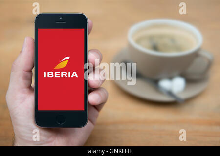 Ein Mann schaut auf seinem iPhone die der Iberia Airline Logo anzeigt, während bei einer Tasse Kaffee (nur zur redaktionellen Verwendung) saß. Stockfoto