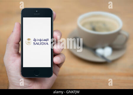 Ein Mann schaut auf seinem iPhone die Saudia Saudi Arabian Airlines Logo, mit einer Tasse Kaffee (nur zur redaktionellen Verwendung) anzeigt. Stockfoto