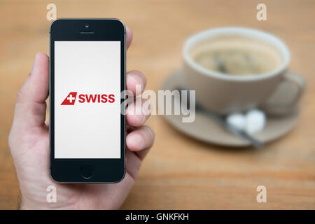 Ein Mann schaut auf seinem iPhone das das Swissair Logo anzeigt, während bei einer Tasse Kaffee (nur zur redaktionellen Verwendung) saß. Stockfoto