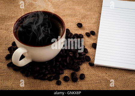 Gesäumt von Papier Tagebuch auf Sackleinen mit Tasse heißen Kaffee und Kaffeebohnen Stockfoto