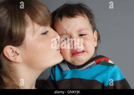 schöne Mutter küssen ihren weinenden Sohn Stockfoto