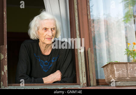 Ältere Frau allein auf ihr Haus Fenster Stockfoto