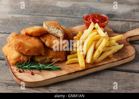Hähnchen-Nuggets Pommes Frites auf dem Brett mit roter Soße Stockfoto