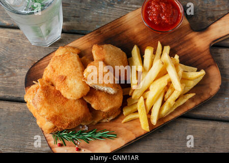 Hähnchen-Nuggets Pommes Frites auf dem Brett mit roter Soße Stockfoto