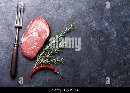 Rohes Rindfleisch Steak Kochen und Zutaten. Stück Fleisch, Kräuter und Gewürze. Draufsicht mit textfreiraum über Steintisch Stockfoto