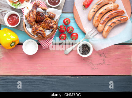 Auswahl an gegrillten Grillfleisch wie Huhn und Würstchen mit Salat auf einem Holztisch Stockfoto