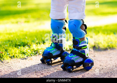 Kleines Mädchen lernen, Rollschuh in sonnigen Sommerpark. Kind trägt Schutz Ellenbogen und Knie-Pads, Handgelenkschutz und Sicherheit Stockfoto