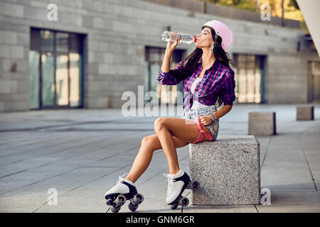 Junge Frau auf Rollschuhen und Helm Trinkwasser Stockfoto