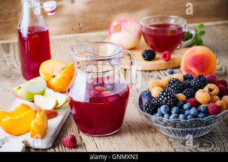 Frische Sommerbeeren und Früchte im Glas Schüssel und Früchte Tee mit Himbeeren, Brombeeren und Heidelbeeren auf Holztisch Stockfoto