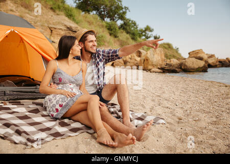 Schönen jungen Mann zeigte auf etwas sitzen mit Freundin im Zelt am Strand Stockfoto