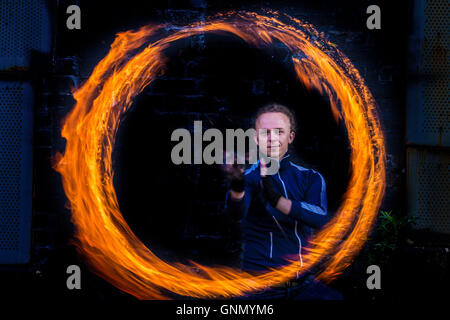 Männliche Feuer Tänzer in Gymwear dreht Poi in Dunkelheit umgeben von Ring des Feuers in der Dämmerung Stockfoto