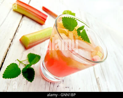 Limonade mit Rhabarber und Minze in ein Glas, den Stielen und Blättern von Rhabarber auf Holzbrettern Hintergrund Stockfoto