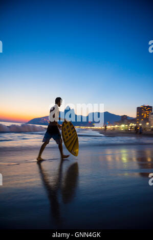 RIO DE JANEIRO - 24. März 2016: Junge Carioca brasilianischen Skimboarder Erhebungen der Sonnenuntergang Wellen am Strand von Ipanema Strand. Stockfoto