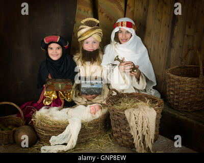 Drei Mädchen spielen als weisen mit einer Puppe in eine Weihnachtskrippe Stockfoto