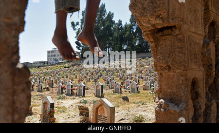 Ein kleiner Junge spielt auf einer Wand mit Blick auf einem Friedhof in Addis Abeba, Äthiopien. Stockfoto