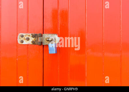 Schloss und Riegel auf eine helle rote geschlossene Holztür Stockfoto
