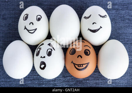 Sieben lustige Eiern mit gezeichneten Gesichter in zwei Reihen, einer ist rot, ein anderes Gesicht ist überrascht, auf grauem Hintergrund Stockfoto