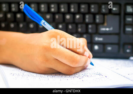 Menschliche Hand mit Stift auf weißem Papier mit Tastatur in den Boden zurück, isoliert, Tiefenschärfe, geringe Schärfentiefe, conce Stockfoto