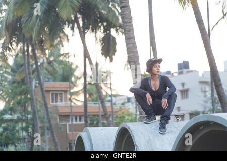 Porträt der indischen weiblichen Skateboarder sitzt man ihr Skateboard auf einer Baustelle mit den Sonnenuntergang im Hintergrund Stockfoto