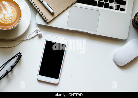 Büro-Zeug mit Smartphone-Laptop und Kaffee Tasse Maus Notizblock auf die weiße Tischplatte Ansicht gedreht. Stockfoto