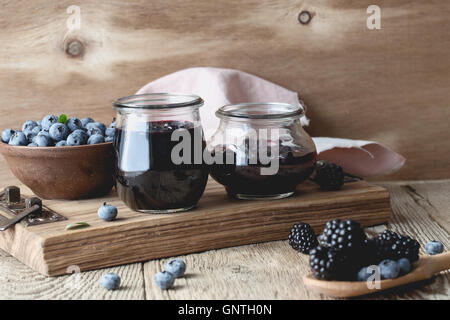 Hausgemachte Blaubeeren und Brombeeren Marmelade in Gläsern und frischen Beeren auf rustikalen Holztisch Stockfoto