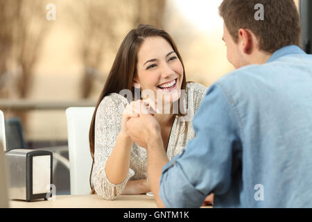 Glückliches Paar Partnersuche und flirten und Hand in Hand zusammen in einem Café mit einem Sonnenuntergang Licht im Freien im Hintergrund Stockfoto